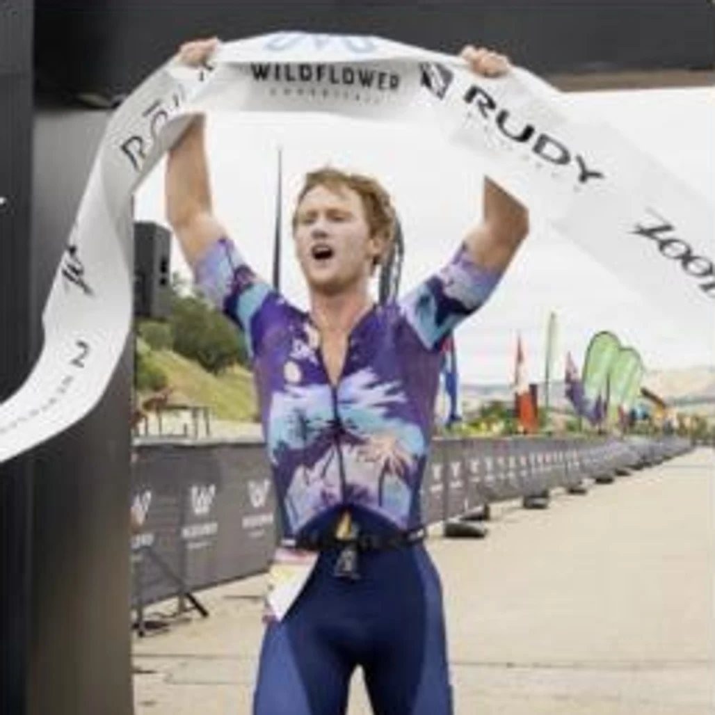 Matthew Quinn breaking the finish tape at the Wildflower Triathlon, arms raised