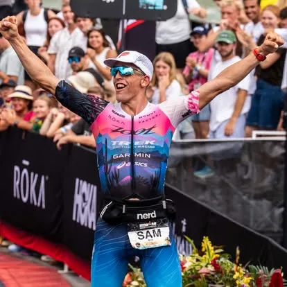 Sam Long celebrating with both arms raised at the IRONMAN World Championship finish in Kona