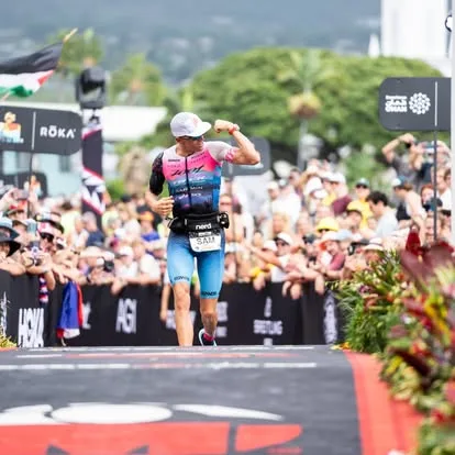 Sam Long flexing as he runs down the Kona finish chute